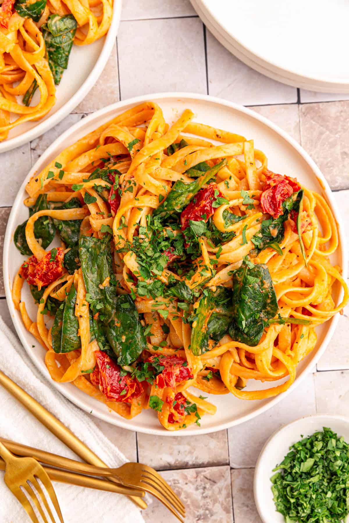 A plate of vegan sundried tomato pasta, garnished with chopped fresh parsley.