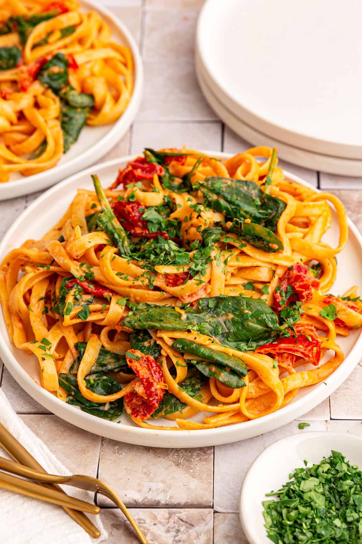A plate of vegan sundried tomato pasta, garnished with chopped fresh parsley.