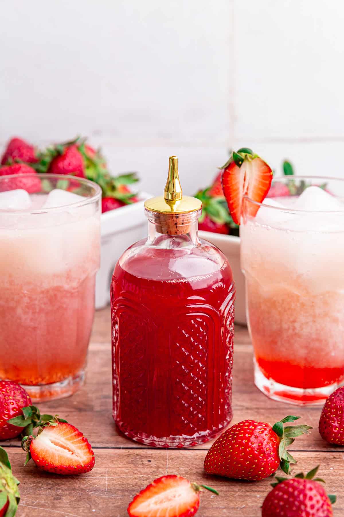A jar of strawberry syrup, next to two jars of strawberry cream soda.