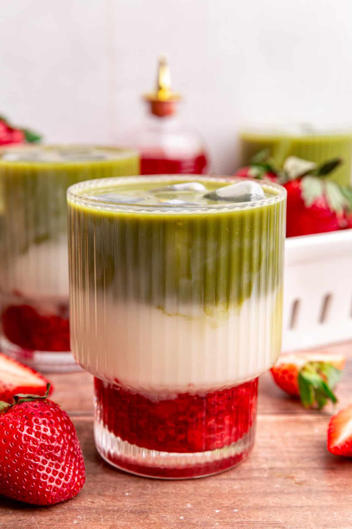 A glass of Strawberry Oat Milk Matcha Latte, with three distinct layers of red syrup, white milk, and green matcha.