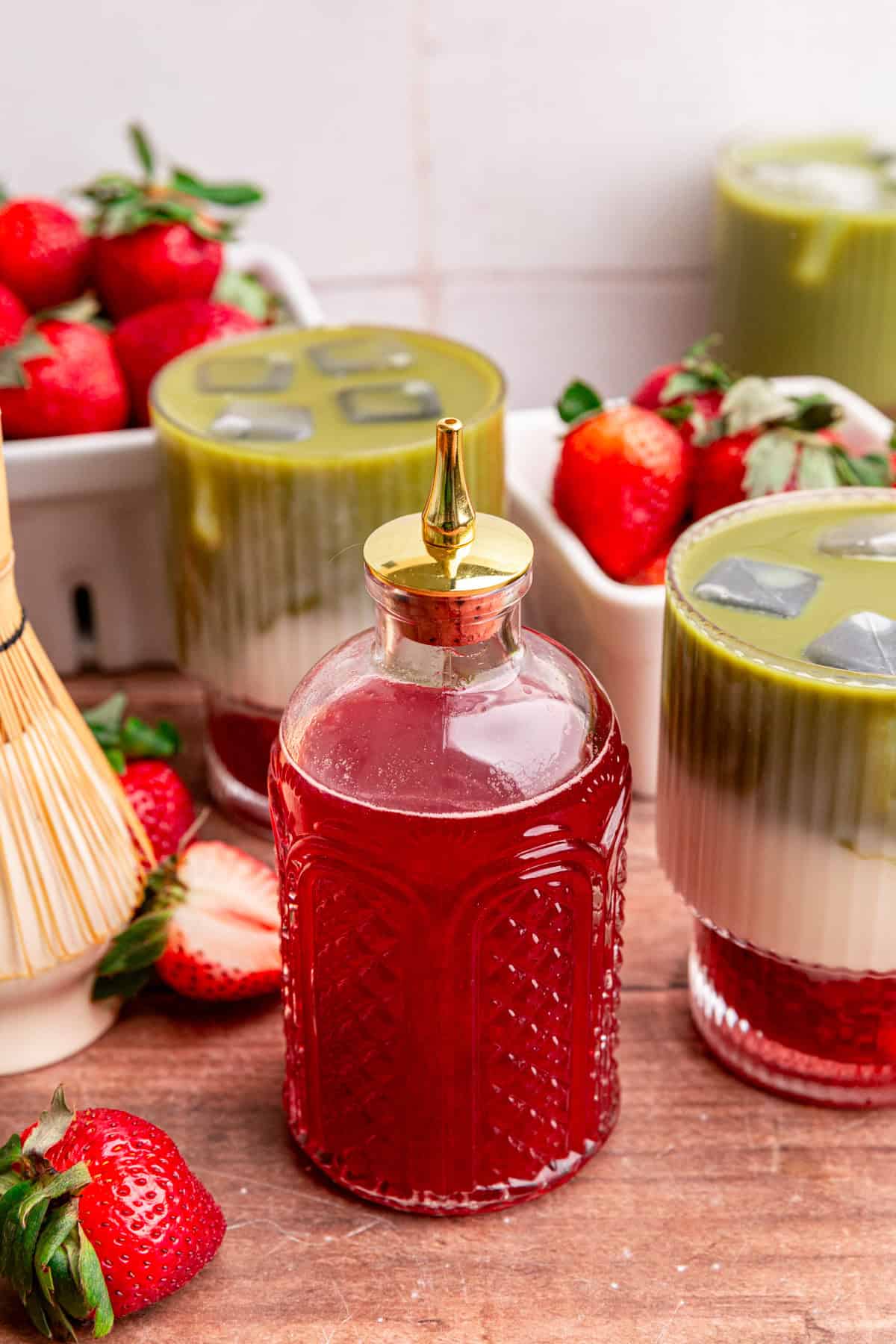 A jar of strawberry simple syrup next to an iced Strawberry Oat Milk Matcha Latte.