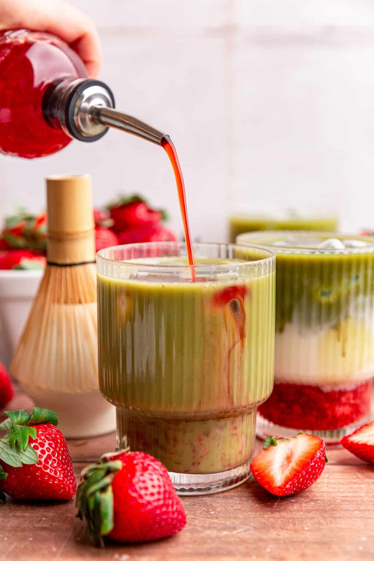Strawberry simple syrup being poured into an iced oat milk strawberry matcha latte that has been mixed, so it's entirely green.