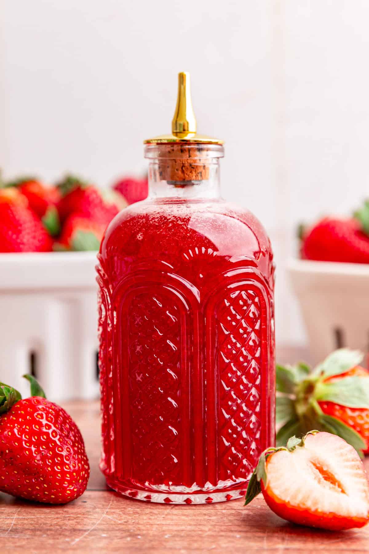 A bitters jar full of strawberry simple syrup, surrounded by fresh strawberries.
