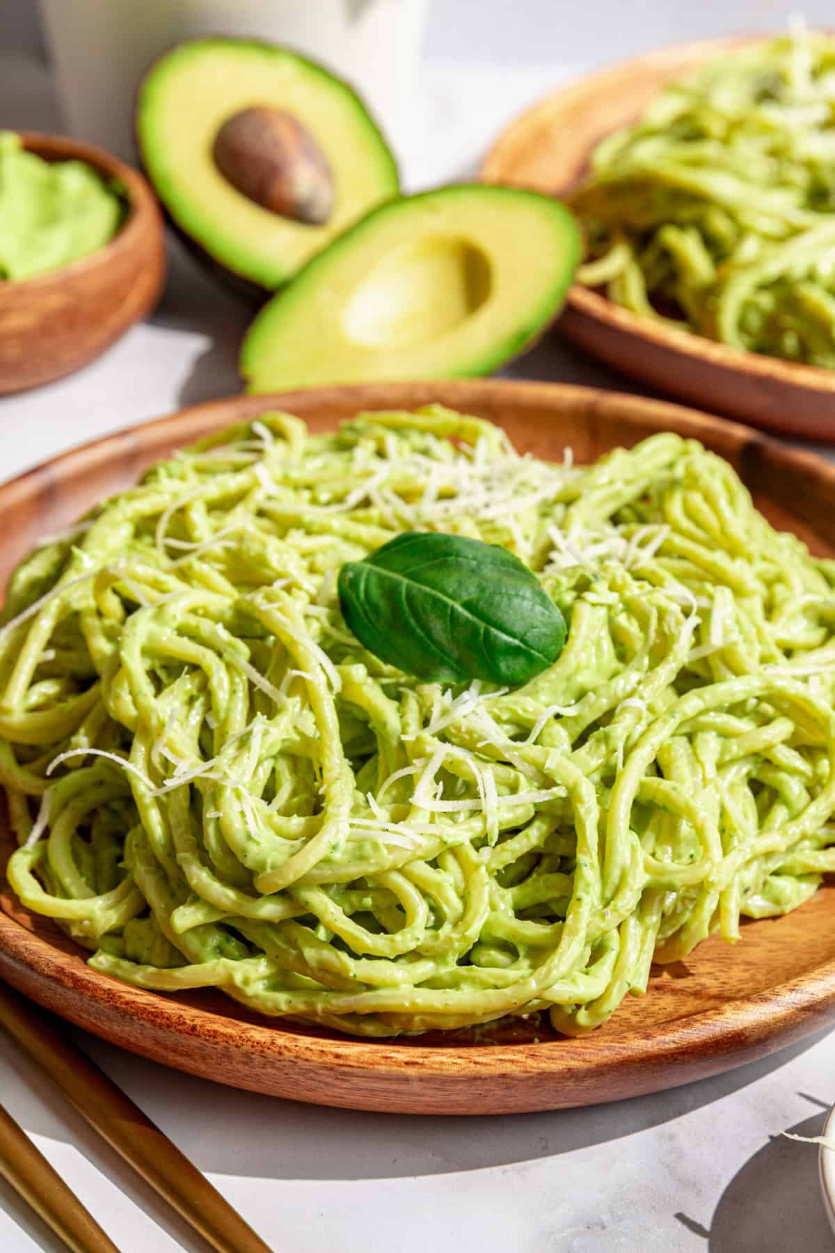 A plate of vegan avocado pasta garnished with vegan parmesan and fresh basil.
