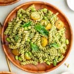 A plate of creamy vegan pesto pasta salad, garnished with fresh basil.