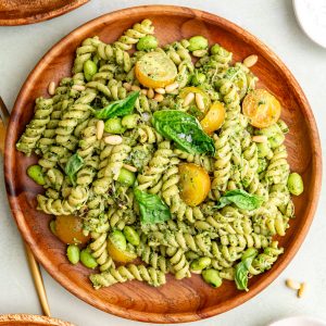 A plate of creamy vegan pesto pasta salad, garnished with fresh basil.