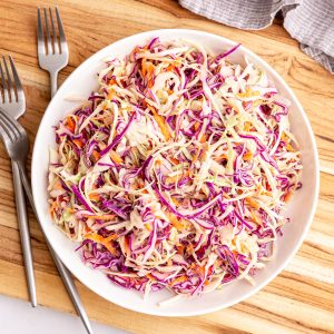 A bowl of vegan coleslaw on a cutting board