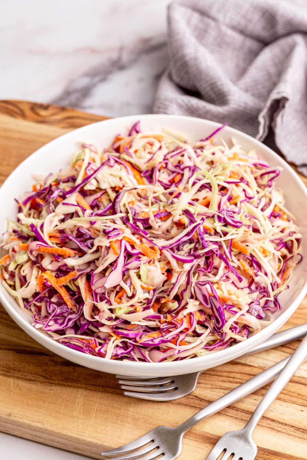 A bowl of vegan coleslaw on a cutting board
