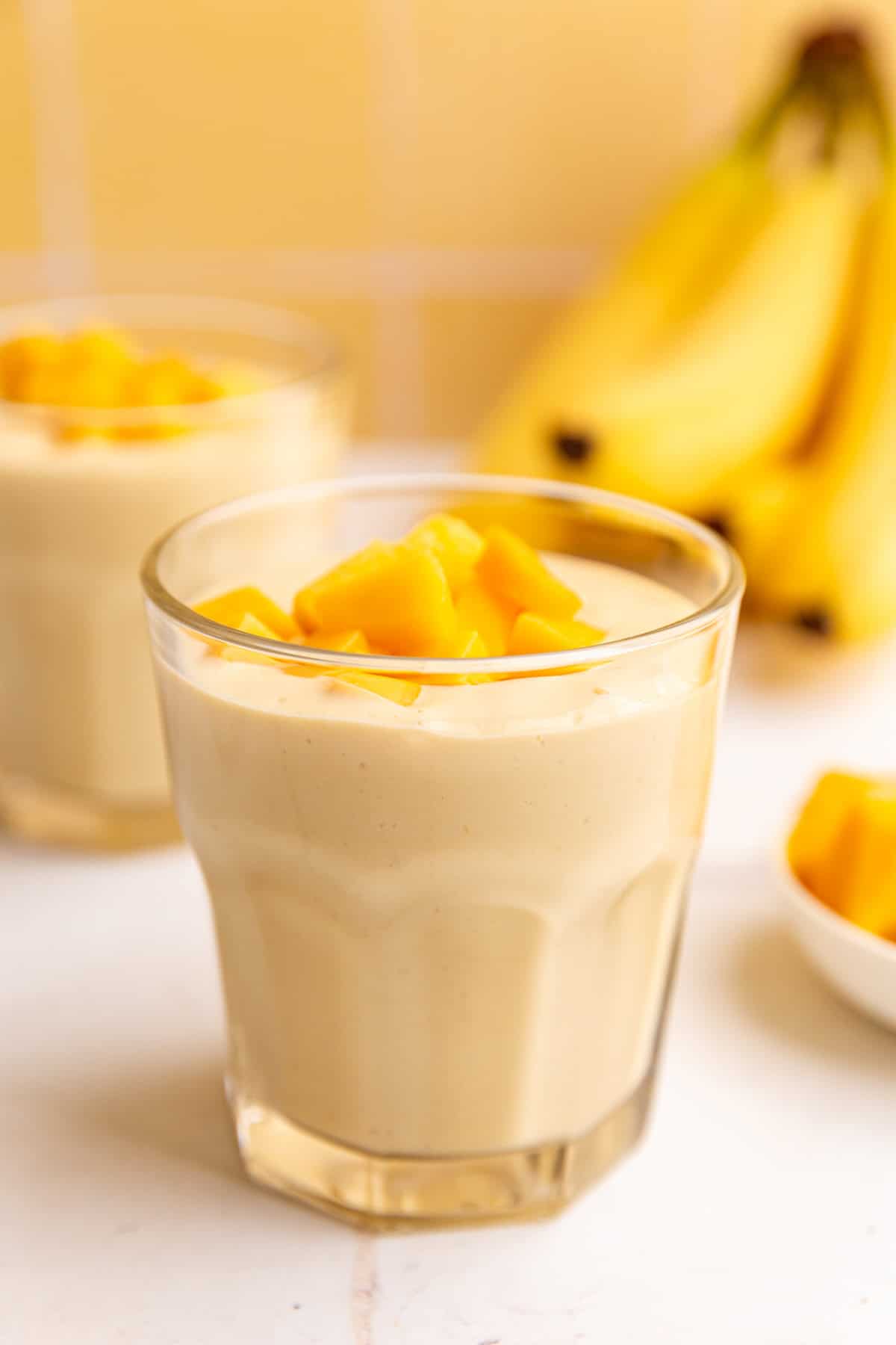 A glass of vegan mango smoothie, topped with mango chunks.