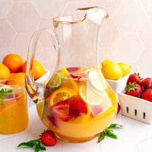 A pitcher of white sangria mocktail with several berry boxes full of fruit.