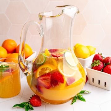 A pitcher of white sangria mocktail with several berry boxes full of fruit.