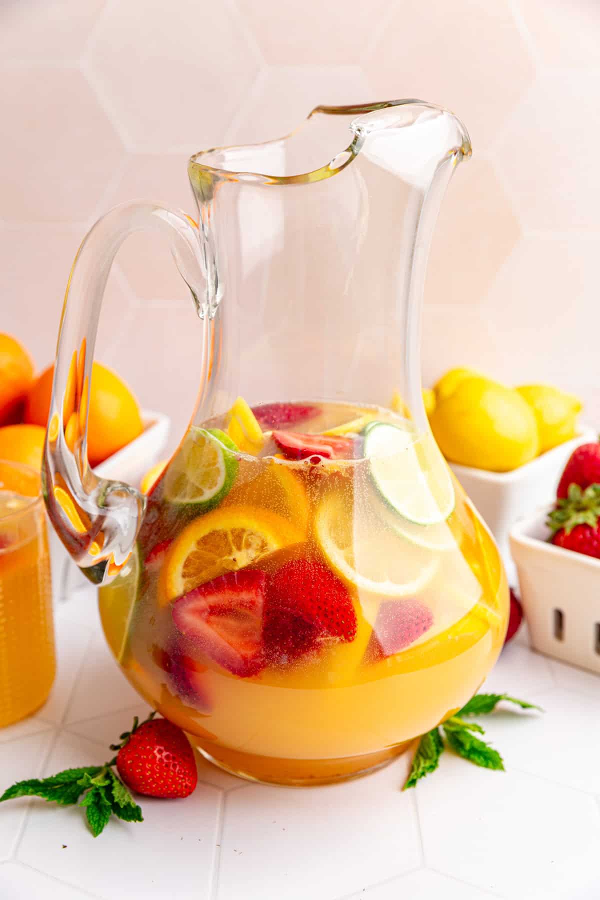 A pitcher of white sangria mocktail with several berry boxes full of fruit.