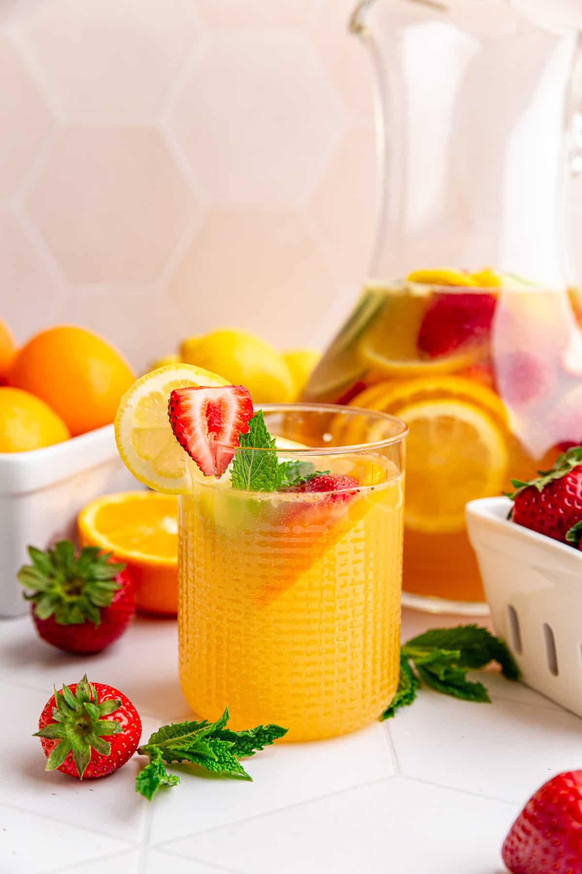 A glass of sangria moctkail next to a pitcher of sangria.