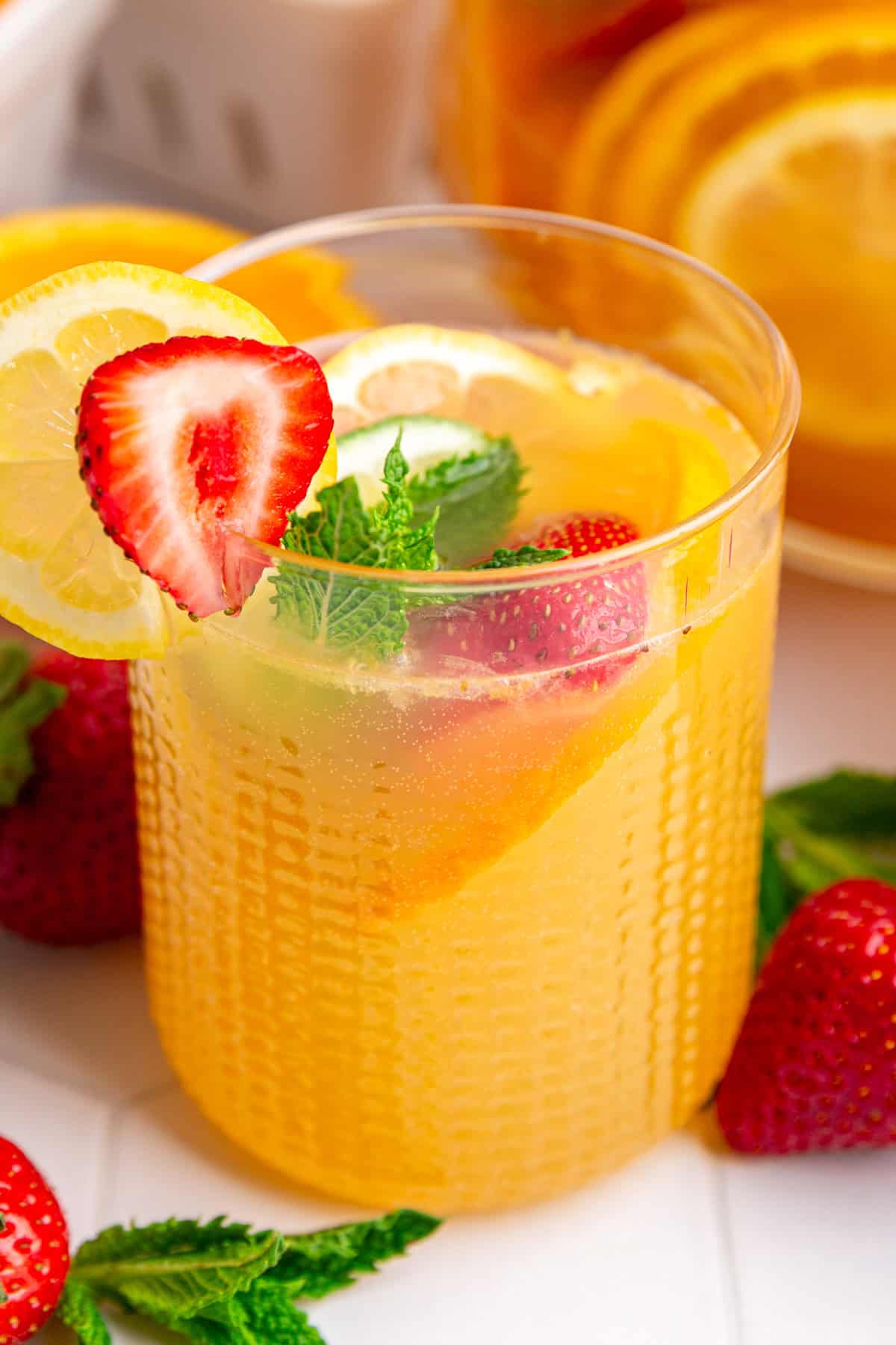 A glass of white sangria mocktail, garnished with a lemon slice and strawbery.