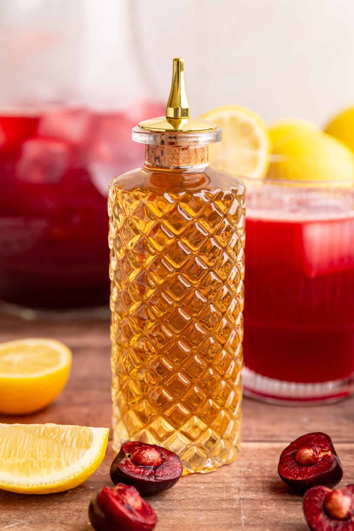 A bottle of agave simple syrup with a glass of cherry lemonade.