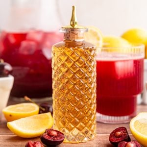 A bottle of agave simple syrup with a glass of cherry lemonade.