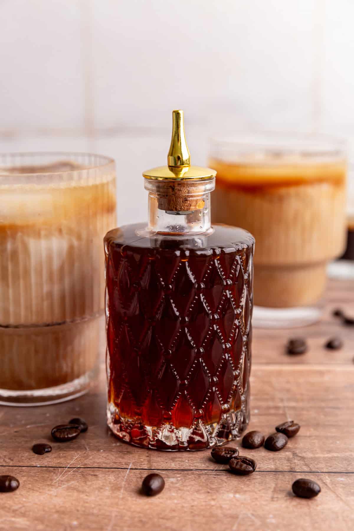 A bitters jar of brown sugar simple syrup with two brown sugar oat milk lattes.