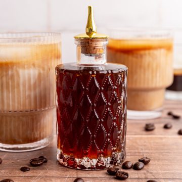 A bitters jar of brown sugar simple syrup with two brown sugar oat milk lattes.
