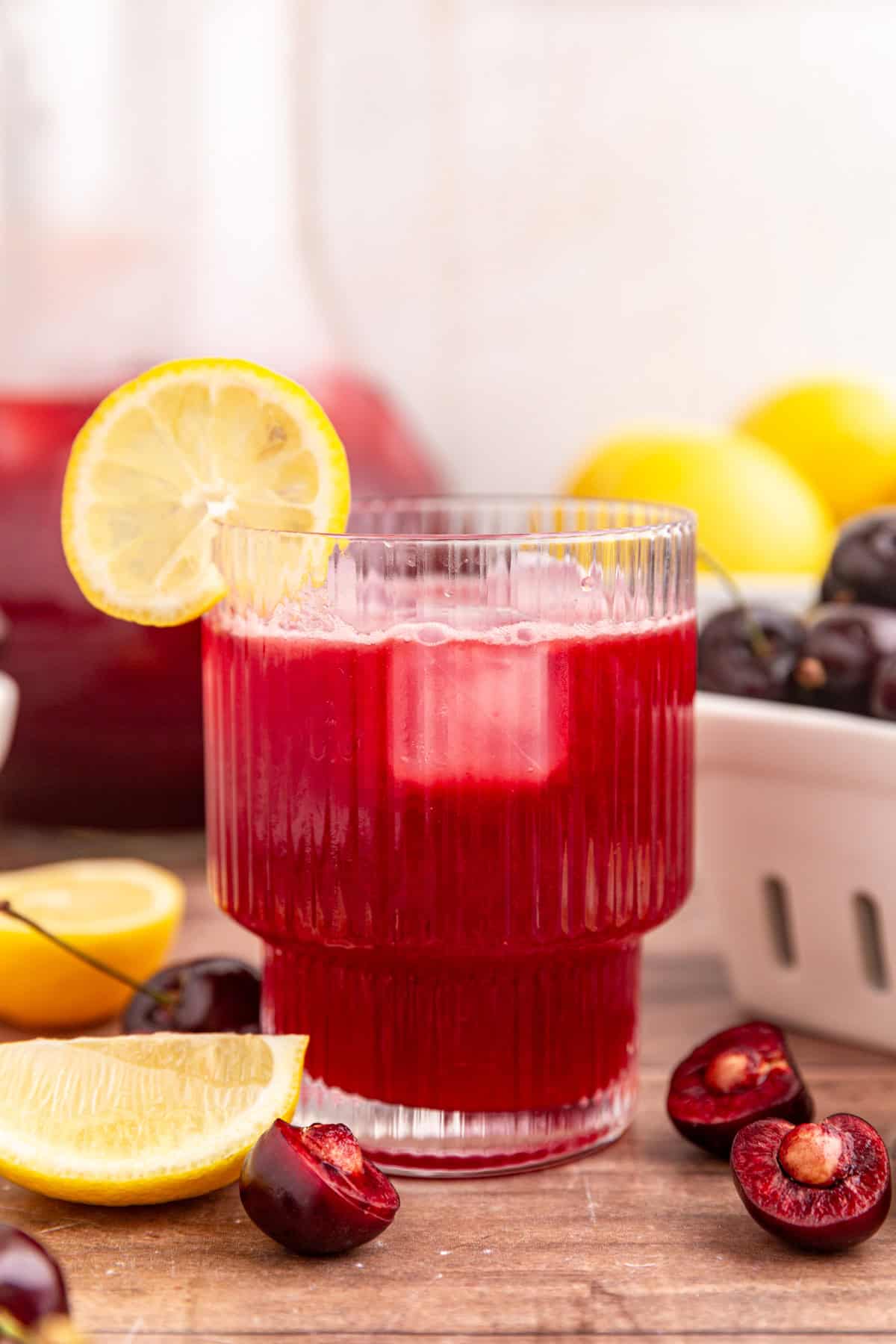 A glass of cherry lemonade garnished with a lemon wedge.