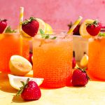 A bubbly glass of Strawberry Pink Lemonade Mocktail, garnished with a sprig of mint, and a strawberry on the rim.