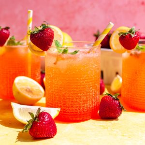 A bubbly glass of Strawberry Pink Lemonade Mocktail, garnished with a sprig of mint, and a strawberry on the rim.