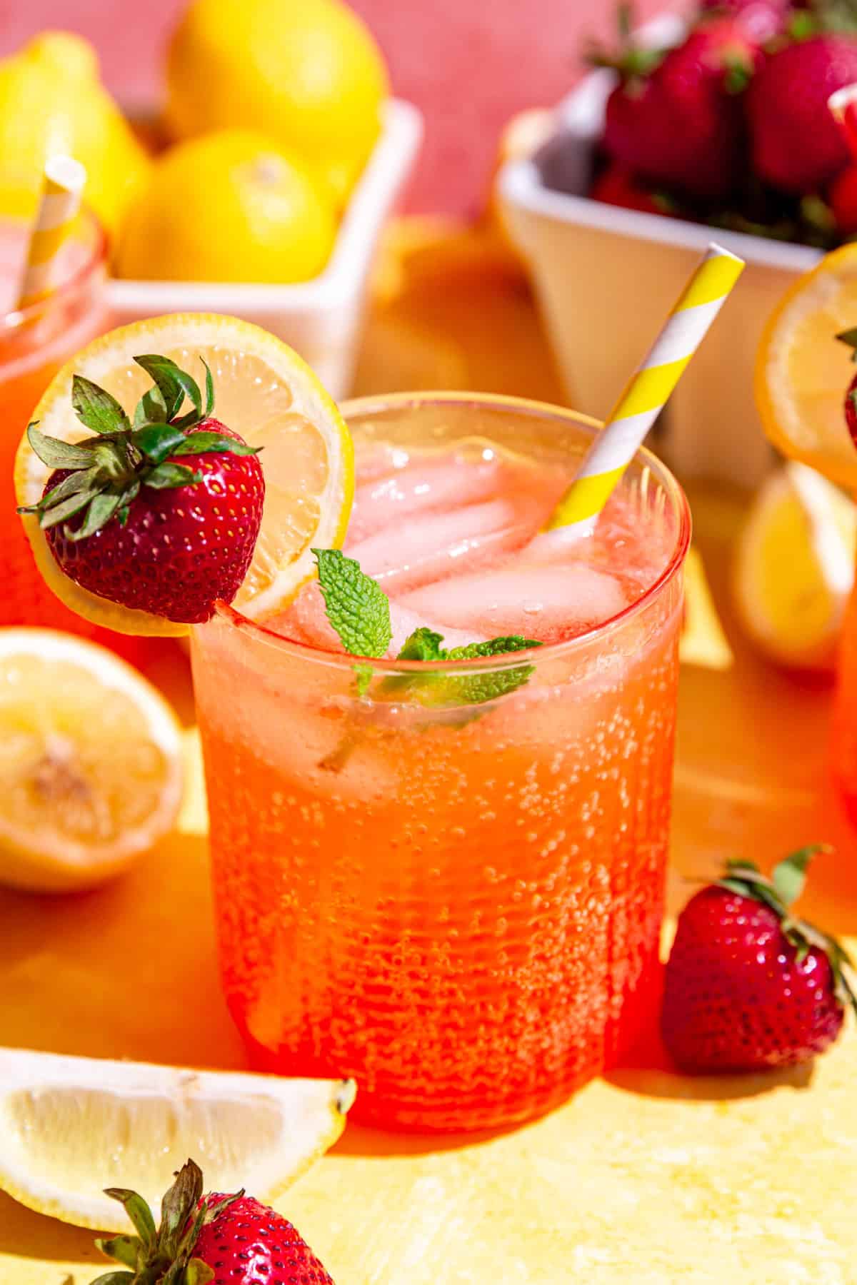 An ice-cold glass of strawberry pink lemonade mocktail, with a yellow and white striped straw.