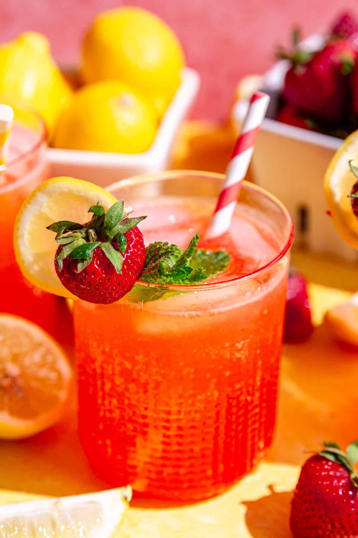 An ice-cold glass of strawberry pink lemonade mocktail, with a pink and white striped straw.