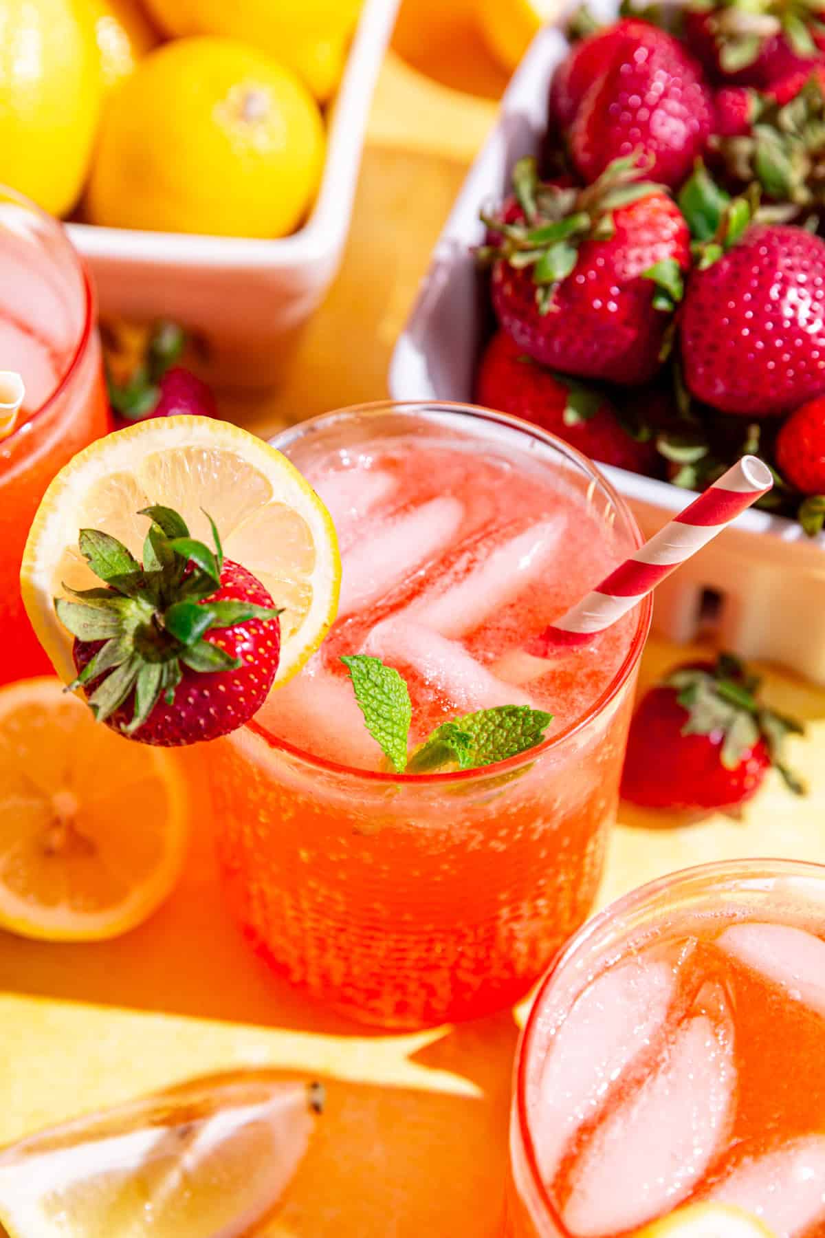 A strawberry lemonade mocktail on a countertop with fresh lemons and strawberries.