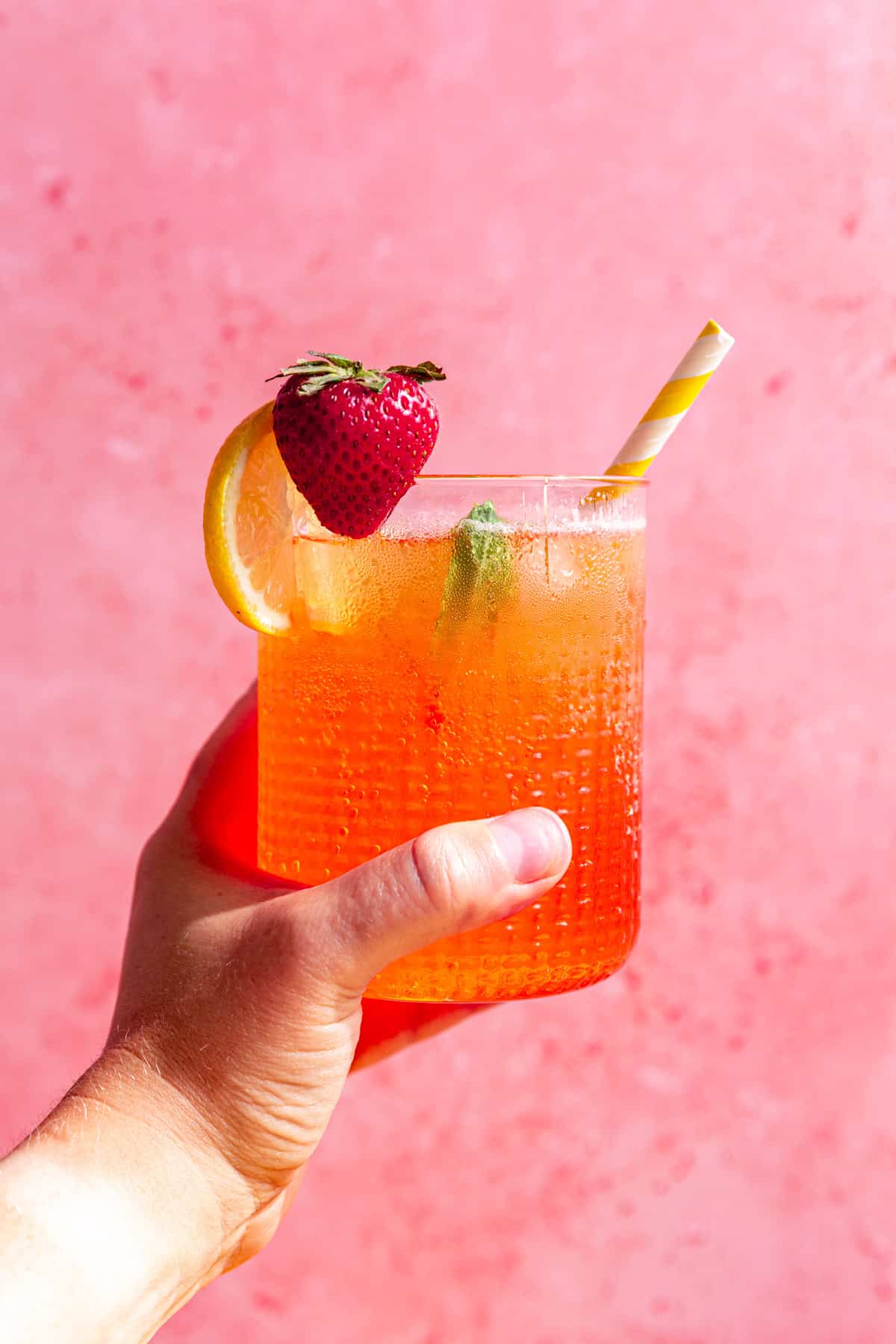 A person holding a strawberry pink lemonade mocktail.