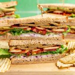 A vegan club sandwich on a cutting board with chips.
