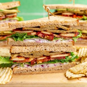 A vegan club sandwich on a cutting board with chips.
