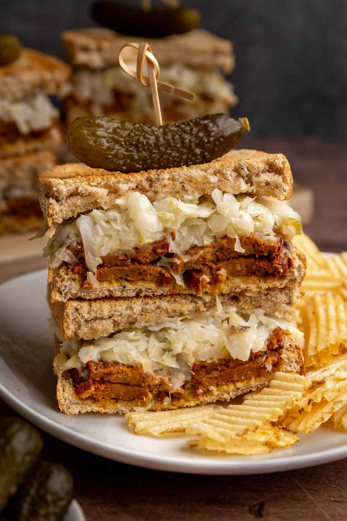 A vegan pastrami sandwich on a plate with potato chips.
