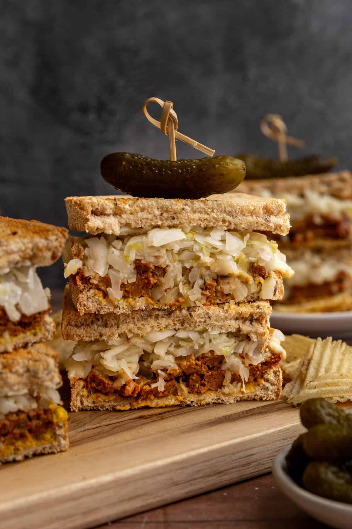Several vegan pastrami sandwiches on a cutting board with potato chips.