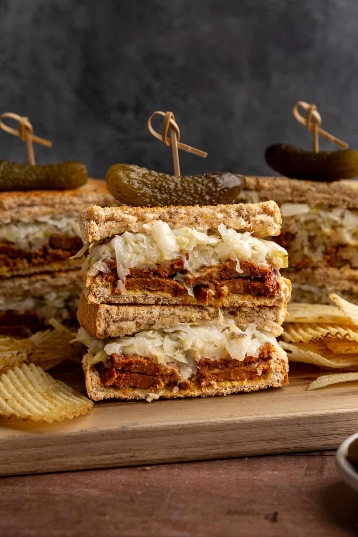 Several vegan pastrami sandwiches on a cutting board with potato chips.