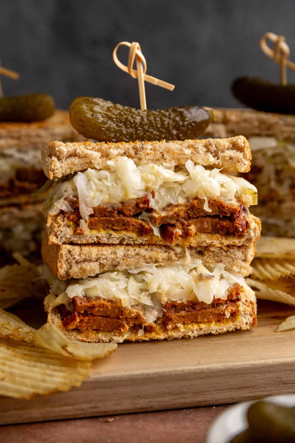 Several vegan pastrami sandwiches on a cutting board with potato chips.