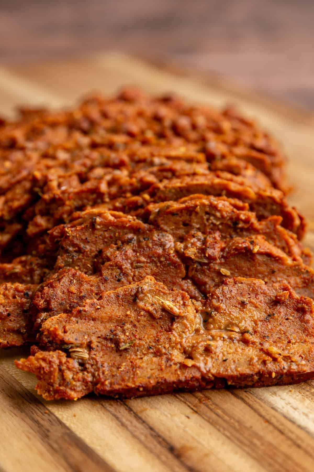 A bath of seitan pastrami sliced on a cutting board.