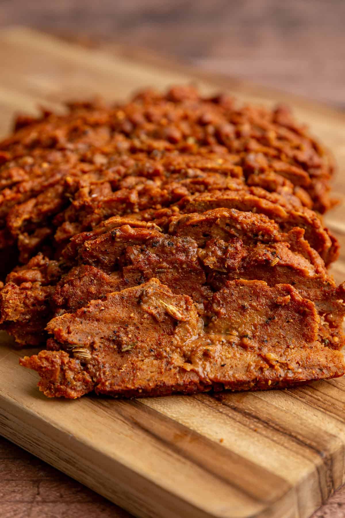 A bath of seitan pastrami sliced on a cutting board.