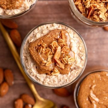 A top-down view of several glasses of almond butter overnight oats, topped with almond butter and vanilla almond granola.