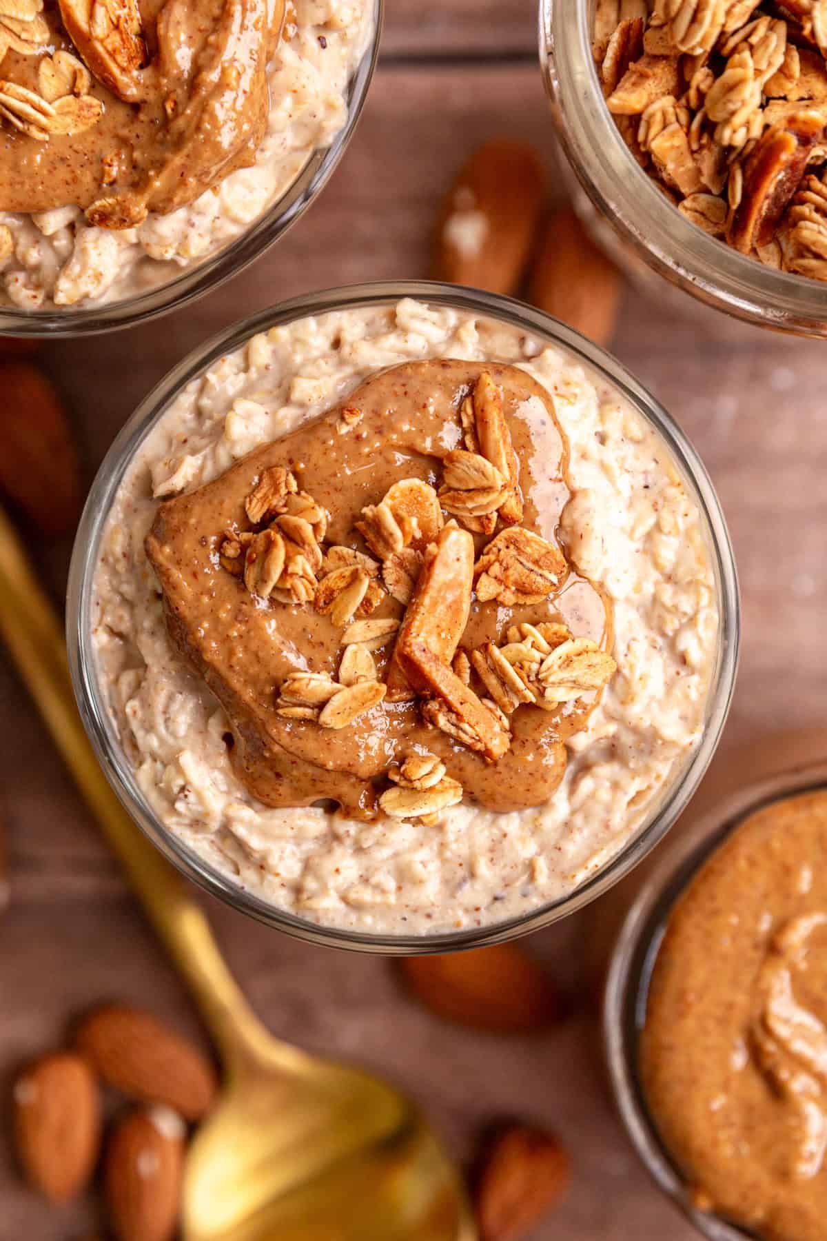 A top-down view of several glasses of almond butter overnight oats, topped with almond butter and vanilla almond granola.