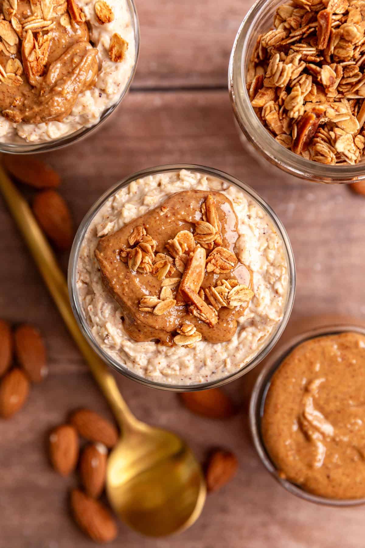 A top-down view of several glasses of almond butter overnight oats, topped with almond butter and vanilla almond granola.