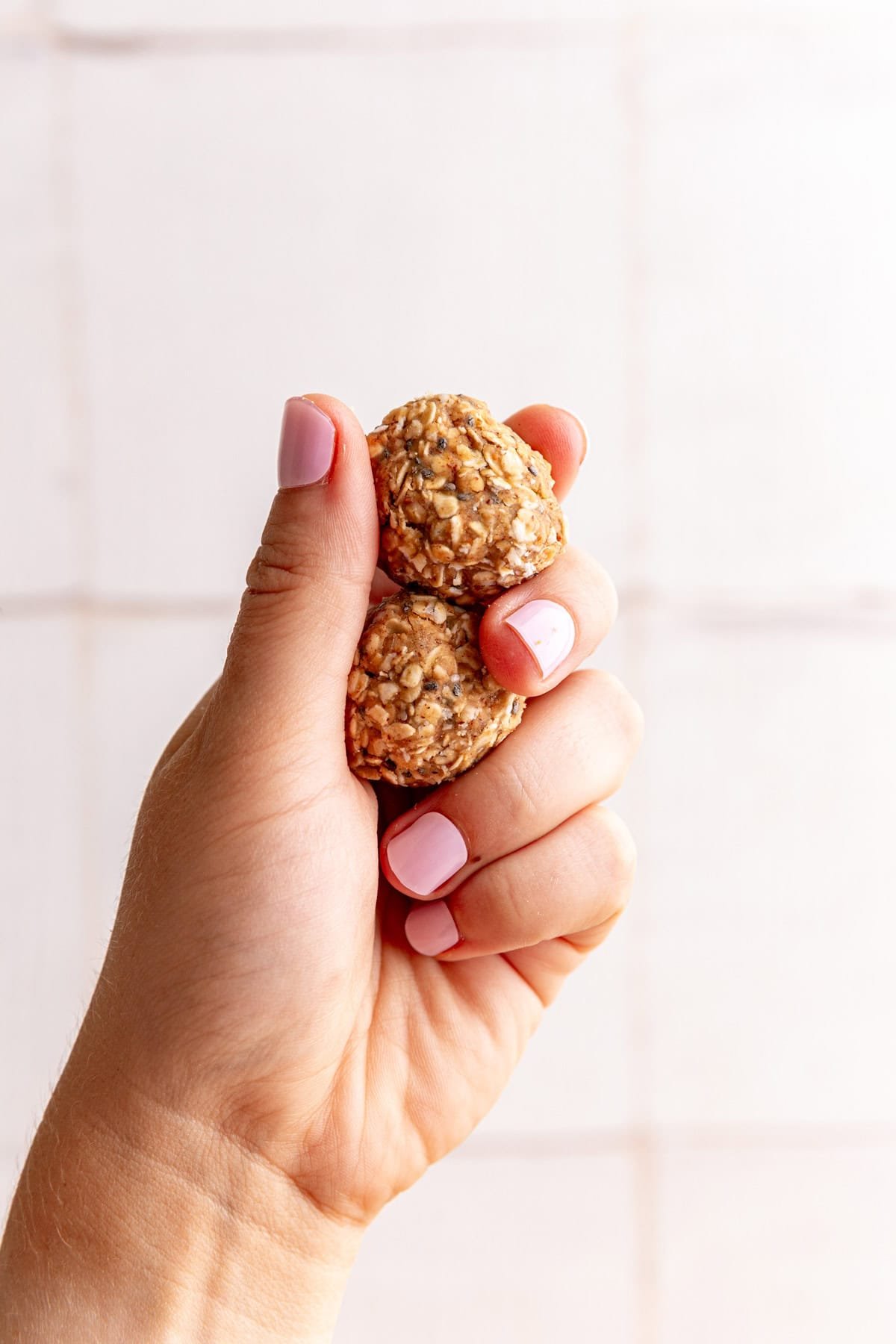 A hand holding two almond butter protein balls.