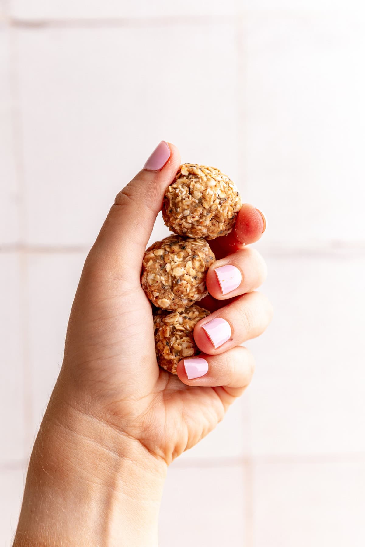 A hand holding three almond butter protein balls.
