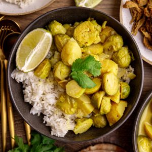 A bowl of brussels sprouts curry with rice and a lime wedge.