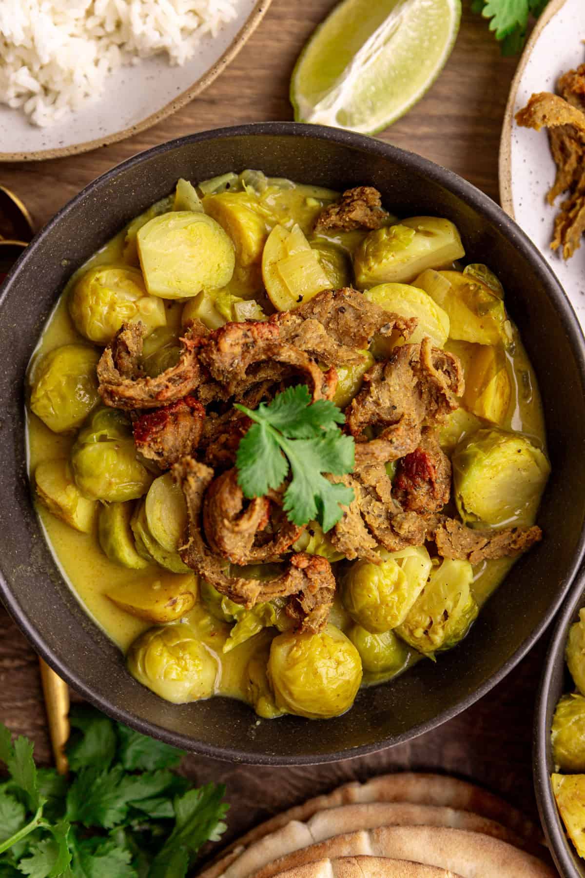 A bowl of brussels sprouts curry topped with seitan chicken and cilantro.