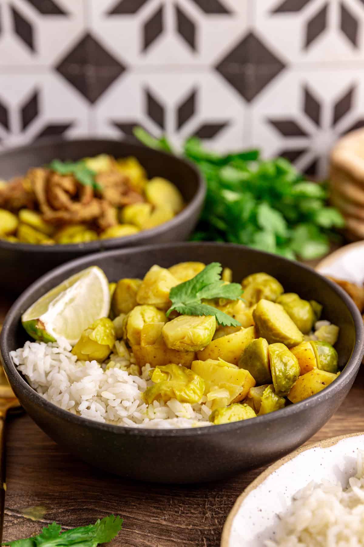 A bowl of brussels sprouts curry with rice and a lime wedge, with other bowls of rice and pita.