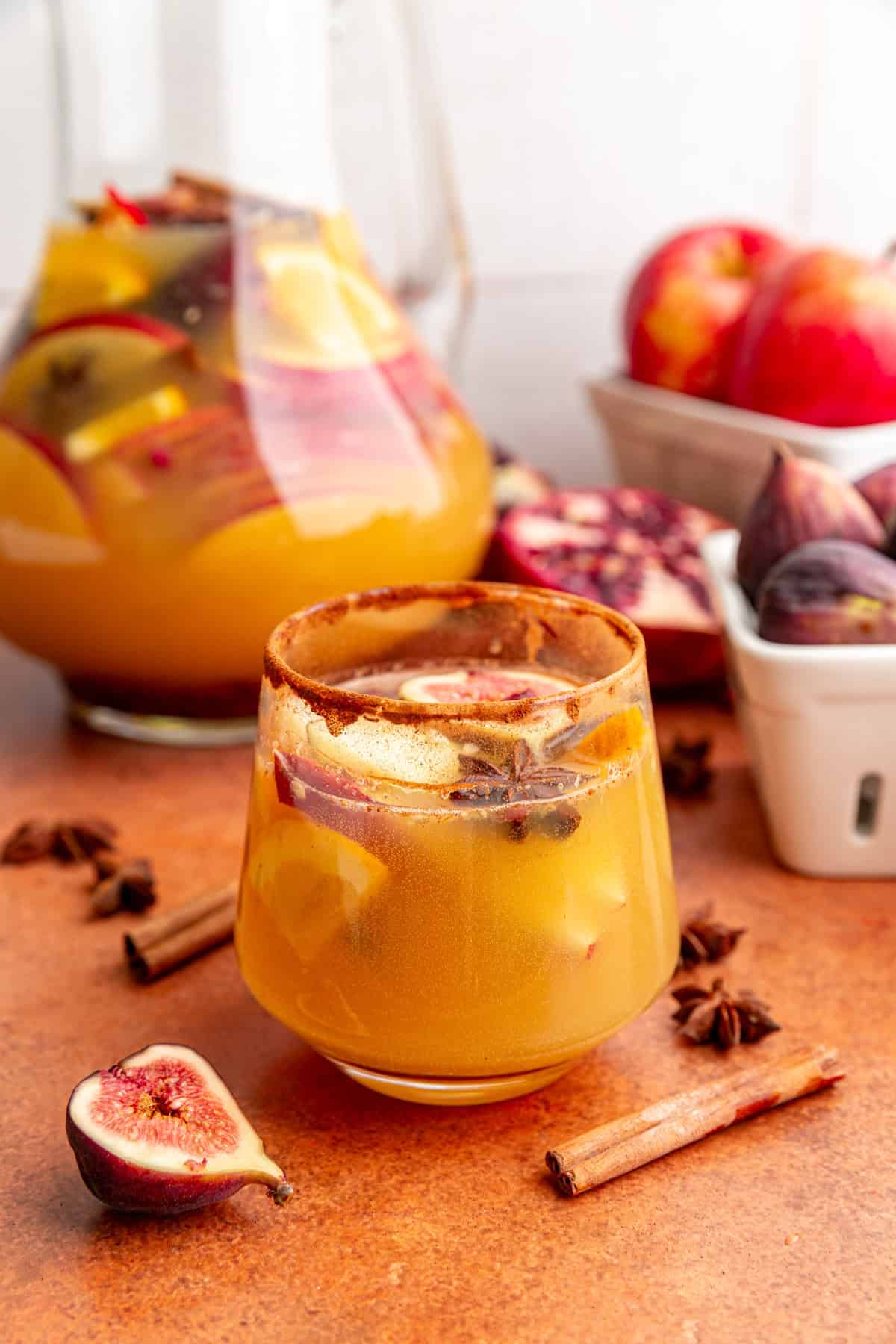 A glass of fall apple cider sangria mocktail sitting next to a pitcher.