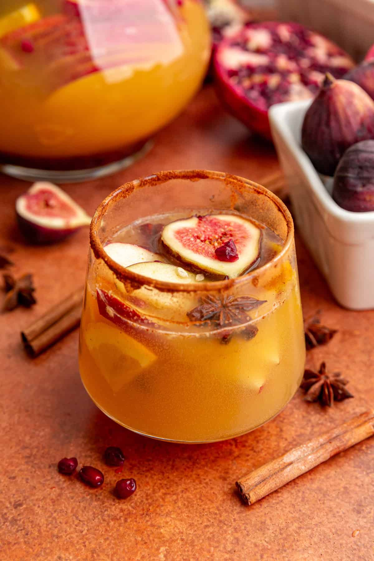 A glass of fall apple cider sangria mocktail, with apple slices, fig, pomegranate, and star anise floating in the drink.