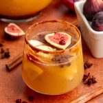 A glass of fall apple cider sangria mocktail, with apple slices, fig, pomegranate, and star anise floating in the drink.