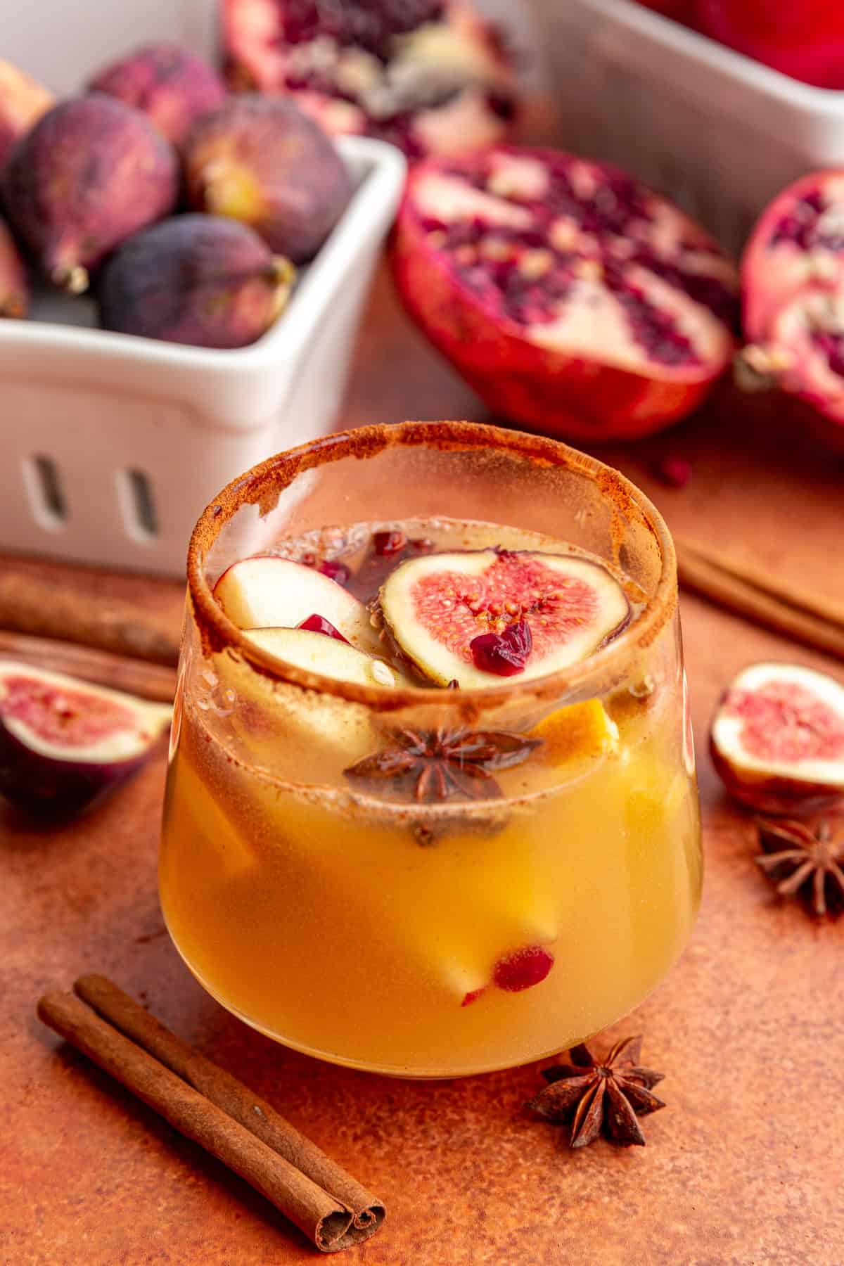 A glass of fall apple cider sangria mocktail, with apple slices, fig, pomegranate, and star anise floating in the drink.