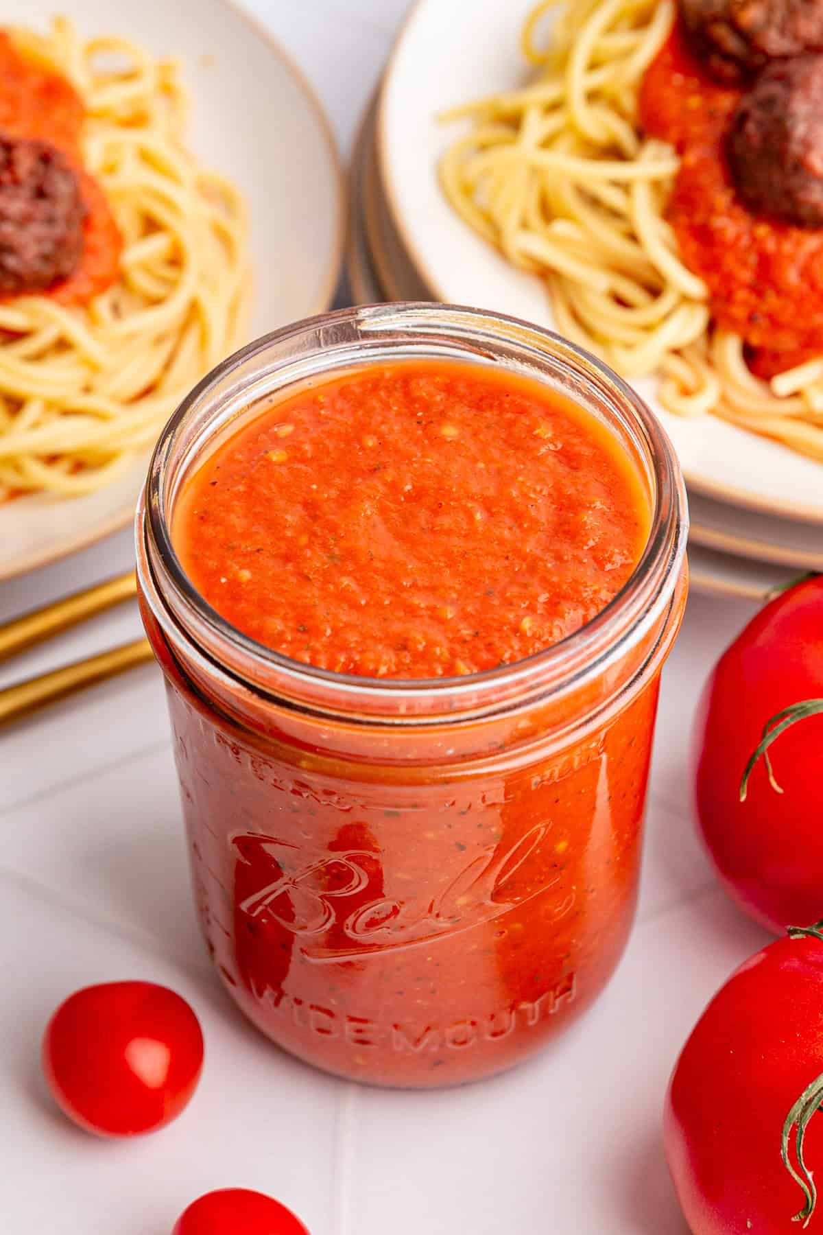 A jar of roasted tomato pasta sauce with two plates of spaghetti and meatballs.